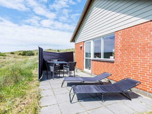 A patio with a table and chairs, two lounge chairs, and a brick building with large windows.