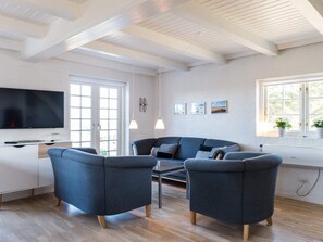 A modern living room with a flat-screen TV, two sofas, a coffee table, and a window with plants. - 5 Star Holiday Home in Norre Nebel (Norre Nebel)