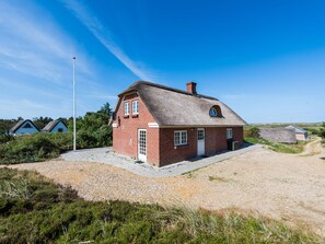 A single-story brick house with a thatched roof, a visible chimney, and a gravel driveway. - 5 Star Holiday Home in Norre Nebel (Norre Nebel)
