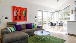 Ein modernes Wohnzimmer mit einem grauen Ecksofa, einem runden Couchtisch und einem farbenfrohen abstrakten Gemälde an der Wand.
