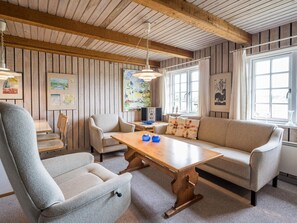 Ein gemütliches Zimmer mit Holzbalkendecke, einer Couch, einem Tisch und Stühlen.