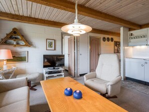 A cozy living room with a wooden table, a television, and a comfortable armchair. - 4 Person Holiday Home in Norre Nebel (Norre Nebel)