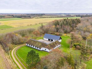 A white building with a thatched roof, surrounded by green fields and trees.