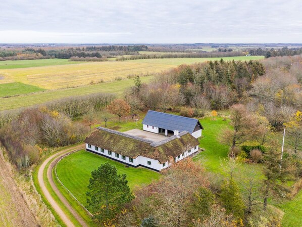 A white building with a thatched roof surrounded by green fields and trees.