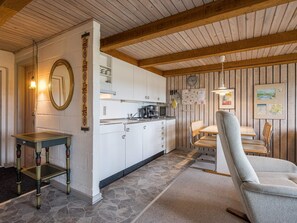 Una cocina compacta con armarios blancos, techo de madera y comedor con mesa y sillas.