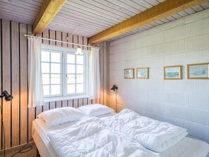 A room with a bed, a window with curtains, a wall with framed pictures, and a ceiling with wooden beams. - 4 Person Holiday Home in Norre Nebel (Norre Nebel)