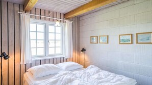 Un dormitorio con techo de madera, una cama con ropa blanca, una ventana con cortinas y tres cuadros en la pared.