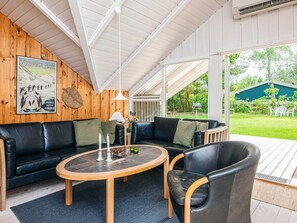 A cozy interior with a wooden ceiling, a black leather sofa, a round wooden table, and a view of a green garden. - 4 Person Holiday Home in Norre Nebel (Norre Nebel)