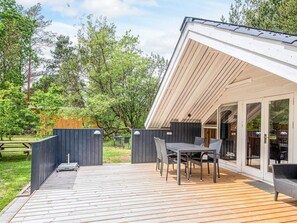 A deck with a table and chairs, a covered area with a sliding door, and a wooden fence. - 4 Person Holiday Home in Norre Nebel (Norre Nebel)