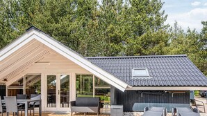 A covered outdoor area with a wooden deck, seating, and a small building with a sloped roof. - 4 Person Holiday Home in Norre Nebel (Norre Nebel)