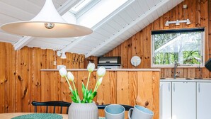 A modern kitchen with wooden walls, a dining area with a round table, and a window with a view of greenery. - 4 Person Holiday Home in Norre Nebel (Norre Nebel)