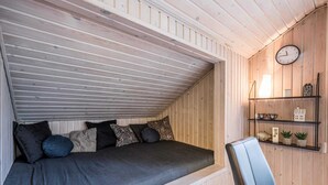 A cozy attic bedroom with a sloped ceiling, a bed with multiple pillows, a chair, a clock, and a shelf with small items. - 4 Star Holiday Home in Norre Nebel (Norre Nebel)