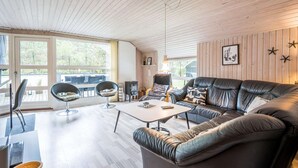 A cozy living room with a leather sofa, a dining table, and a chair. There is a large window providing a view of the outdoors. - 4 Star Holiday Home in Norre Nebel (Norre Nebel)