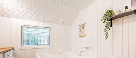 A bathroom with a built-in bathtub, a toilet, a washing machine, and a window with a view of trees.