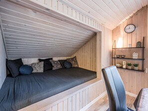 A loft bedroom with a sloped ceiling, a bed with multiple pillows, a chair, a clock, and a shelf with decorative items.