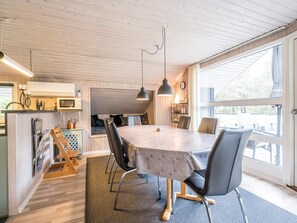 A modern kitchen with wooden cabinetry, a dining area with a large table and chairs, and a view through a large window. - 4 Star Holiday Home in Norre Nebel (Norre Nebel)