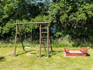Children can play and climb on the swing set and sandbox in this peaceful outdoor space surrounded by lush greenery.