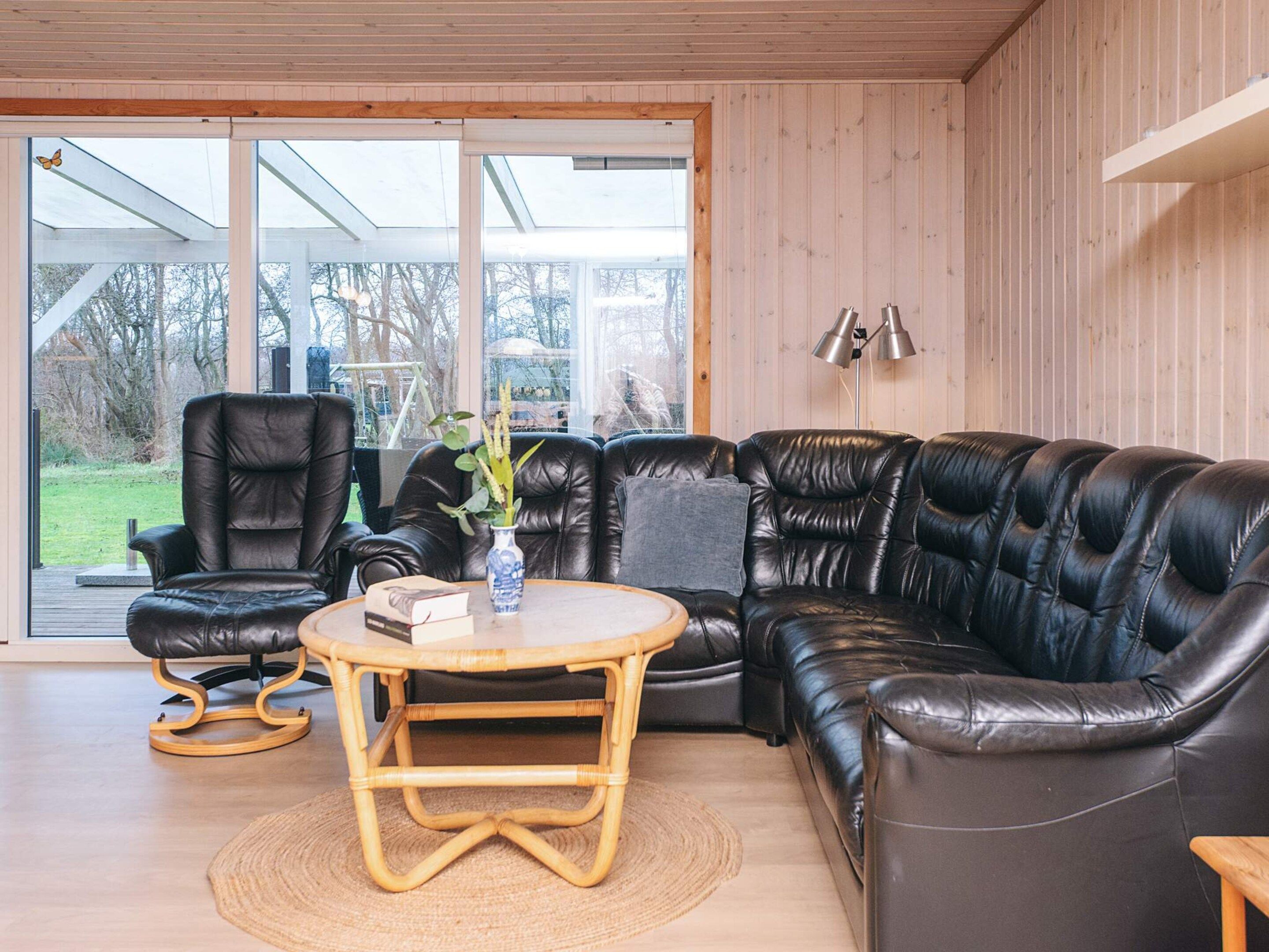A modern living room with a black leather sofa, a wooden coffee table, and a wicker chair.