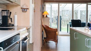 Ett modernt kök med en kaffemaskin, en flätstol och utsikt över naturen genom stora fönster.