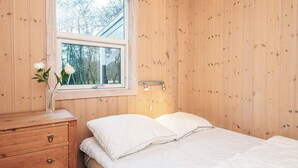 Ett rum med träpanel, en säng, ett nattduksbord, en byrå och ett fönster.