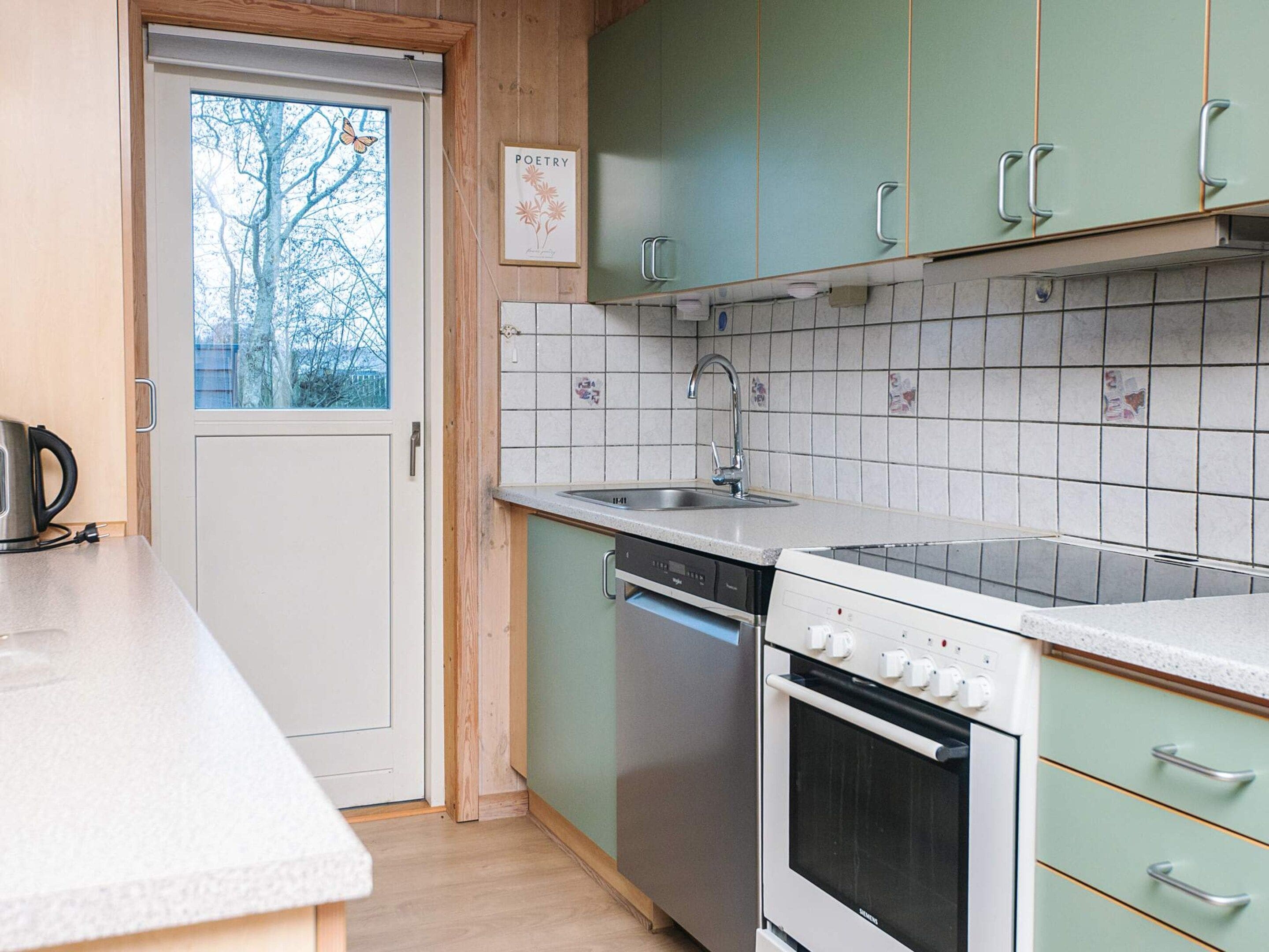 A kitchen with a dishwasher, oven, and a window with a view of trees.