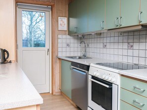 A kitchen with a dishwasher, oven, and a window with a view of trees. - 5 Star Holiday Home in Fano (Fano)