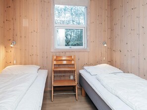 Una habitació petita amb dos llits, una cadira de fusta, una finestra i dues làmpades penjades a la paret.