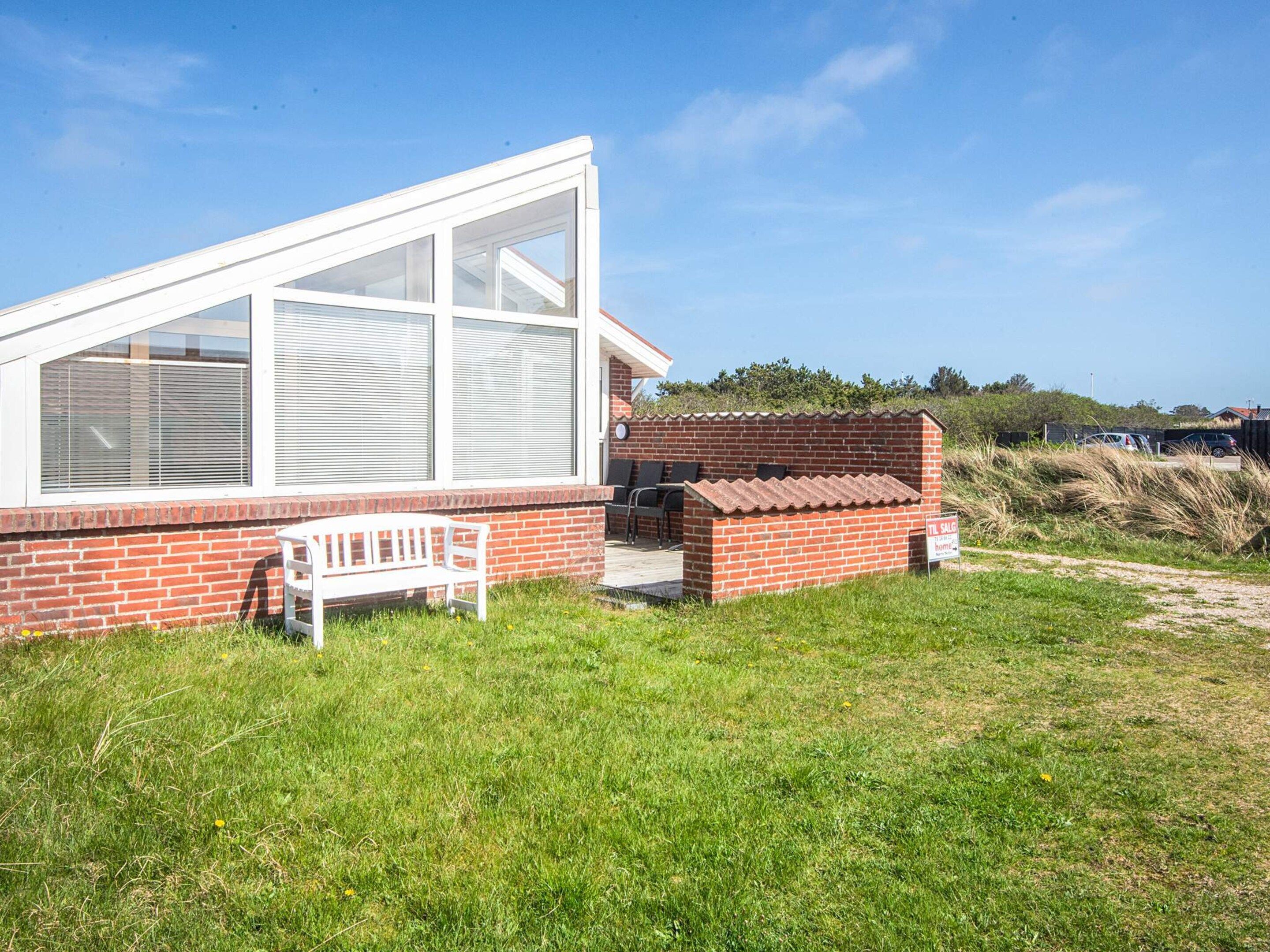 A single-story building with a large glass window, a brick exterior, and a white bench.