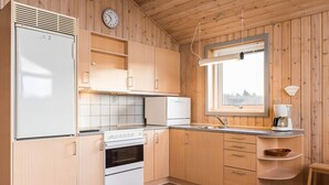 A compact kitchen with wooden cabinets, a built-in oven, a refrigerator, and a window providing natural light. - 4 Person Holiday Home in Henne (Henne)