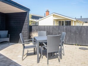 An outdoor patio with a table and four chairs, a wooden fence, and a building in the background.