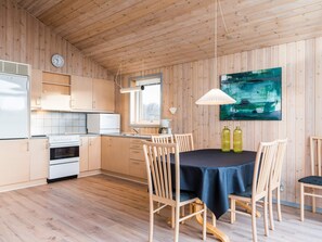 A modern kitchen with wooden cabinets, a dining table with chairs, and a large abstract painting on the wall.