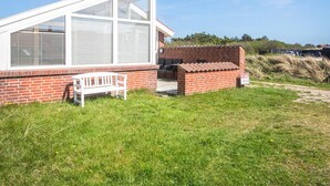 A single-story building with a large glass window, a brick exterior, and a white bench. - 4 Person Holiday Home in Henne (Henne)