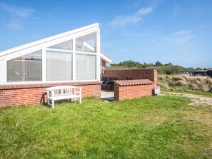 A single-story building with a large glass window, a brick exterior, and a white bench. - 4 Person Holiday Home in Henne (Henne)
