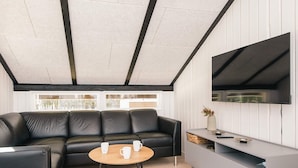 Un salon moderne avec un canapé en cuir noir, une table basse en bois et un meuble de rangement gris intégrant un téléviseur à écran plat.