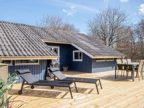 A wooden deck with lounge chairs and a table, a covered outdoor area, and a building with a sloped roof.