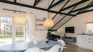 Une cuisine moderne avec des meubles blancs, une table à manger entourée de chaises blanches et une grande fenêtre donnant sur un jardin.