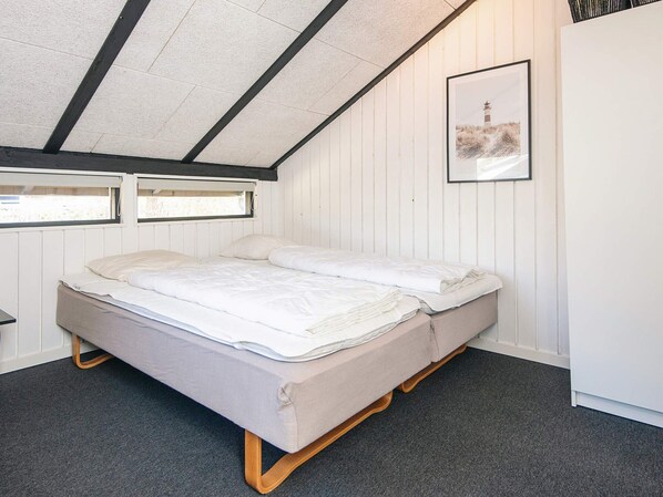 A single bed in a room with a sloped ceiling, a framed picture on the wall, and a window with a view of the outdoors.