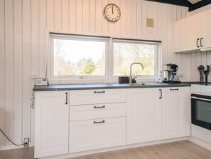 A kitchen with white cabinetry, a double sink, a coffee maker, and a clock on the wall.