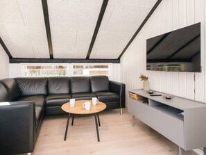 A modern living room with a black leather sofa, a wooden coffee table, and a grey entertainment unit with a flat-screen TV.
