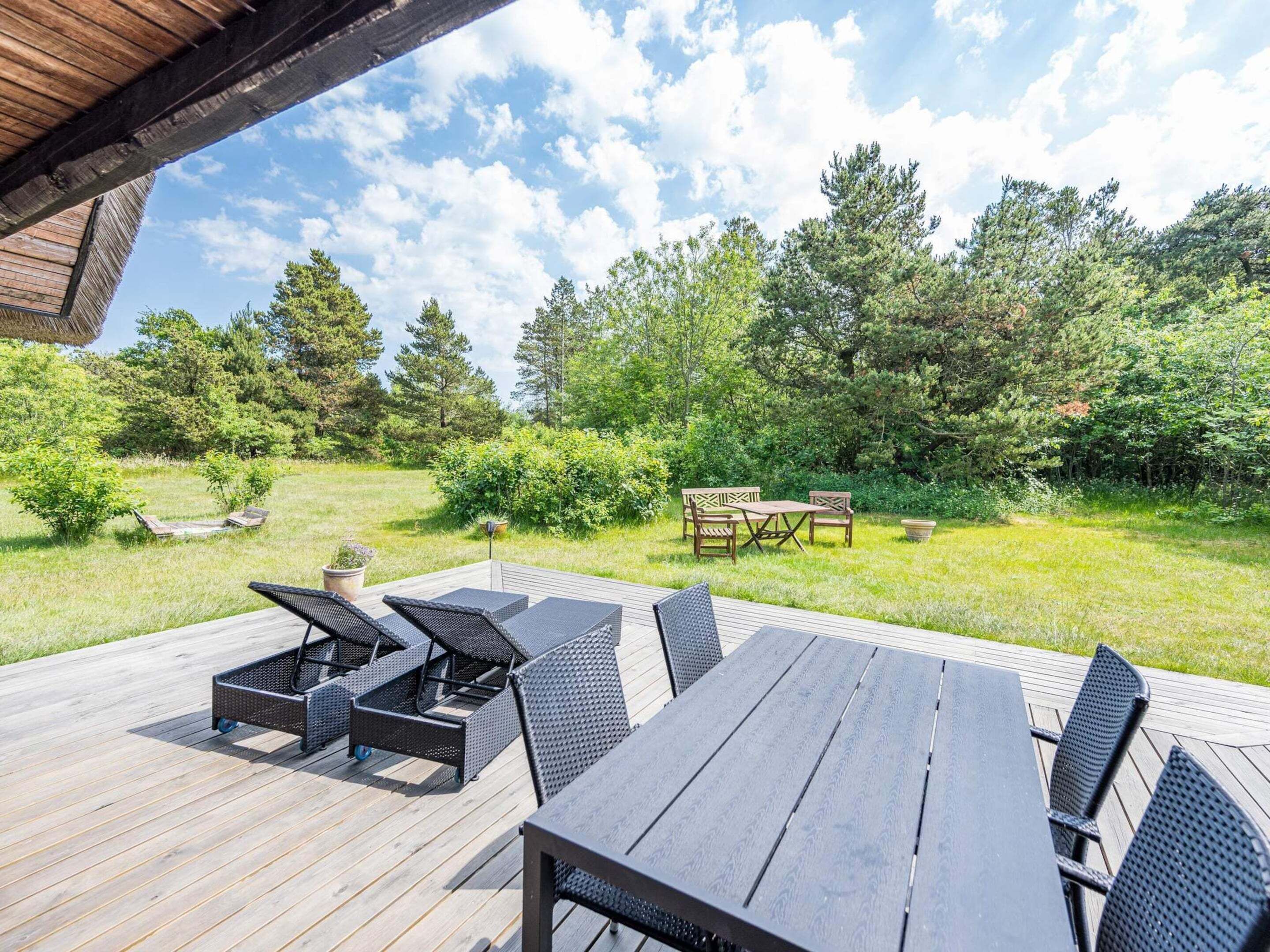 A wooden deck with outdoor furniture, including a table and chairs, surrounded by greenery and trees.