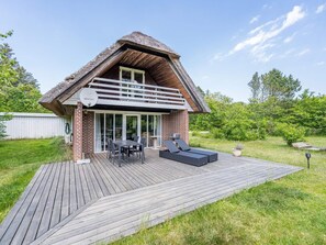 Uma casa moderna com telhado de palha, um deck e um alpendre com móveis de exterior.