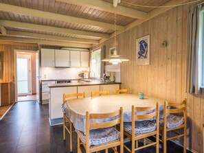 A wooden interior with a kitchen and dining area, featuring a round table with chairs and a wooden ceiling. - 6 Person Holiday Home in Henne (Henne)