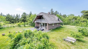 A thatched-roof house with a balcony, surrounded by lush greenery and a clear sky. - 6 Person Holiday Home in Henne (Henne)