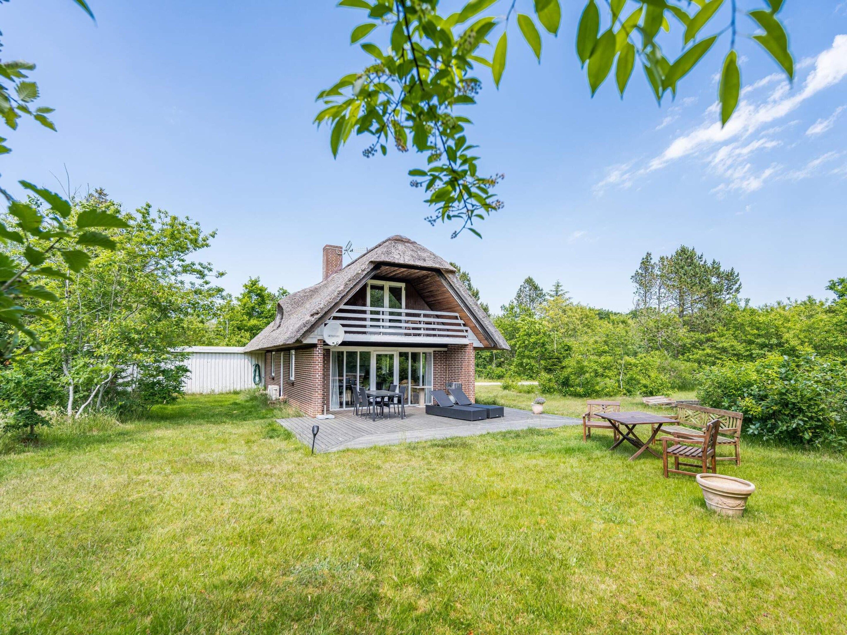 Une maison à toit de chaume avec un patio, entourée de verdure.