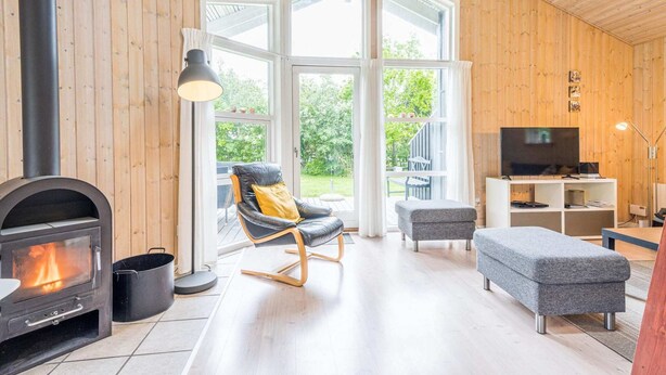 Un salon chaleureux avec une cheminée, un fauteuil confortable, un pouf gris et un téléviseur.