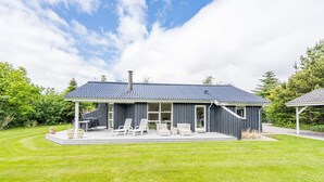 Une maison moderne dotée d’un patio couvert, d’une cheminée et d’une pelouse bien entretenue.