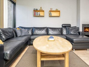 Un salon moderne avec un canapé d’angle en cuir noir, une table basse ronde en bois et une cheminée.