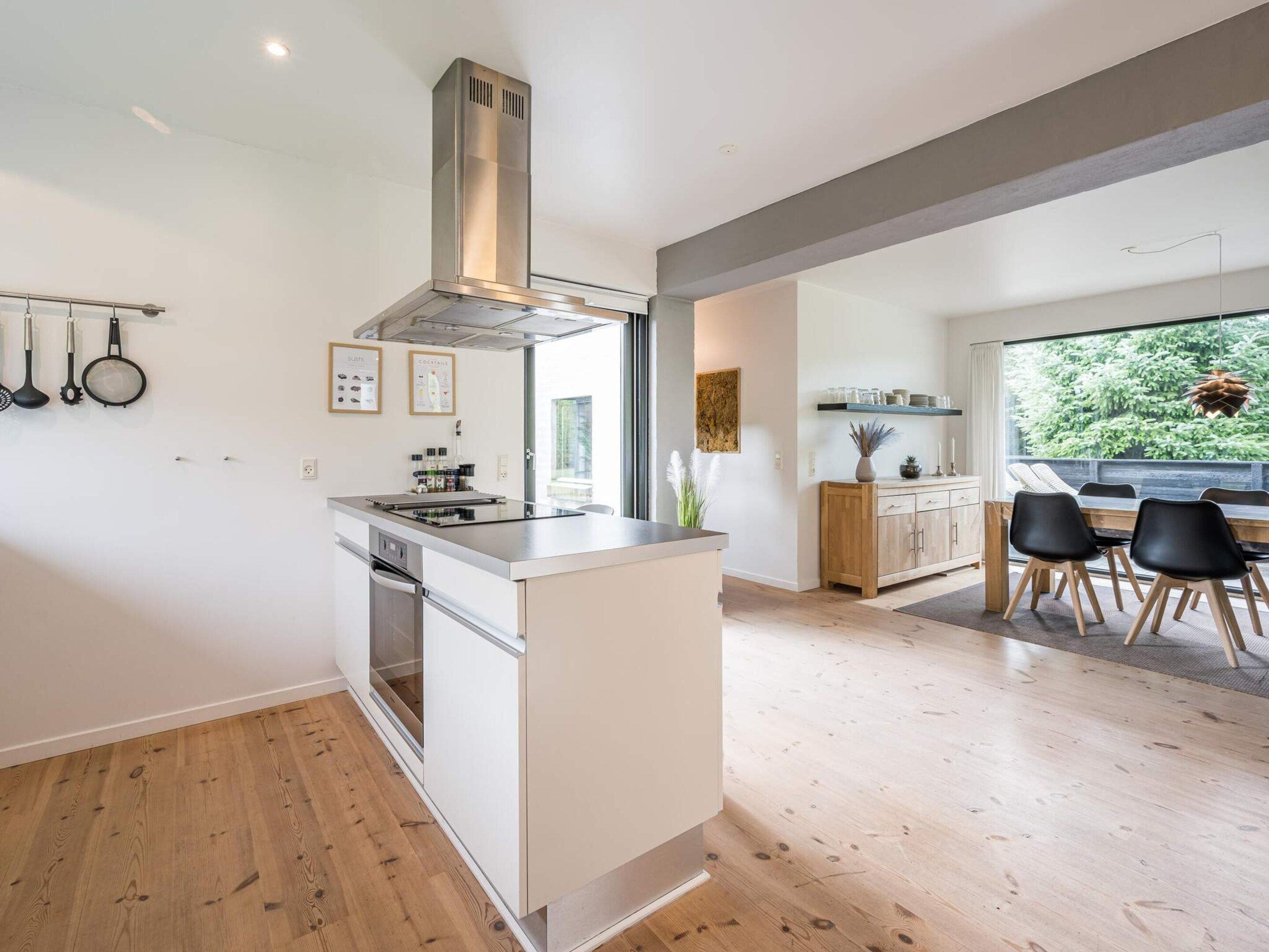 A modern kitchen with a central island, a dining area with a view, and a large window.