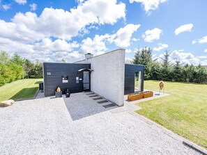 A modern building with a black exterior, a numbered door, and a small garden area with a fire pit and planters.