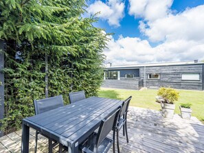 Une terrasse extérieure moderne, dotée d’une table et de chaises, entourée d’une végétation luxuriante et avec un bâtiment contemporain en arrière-plan.